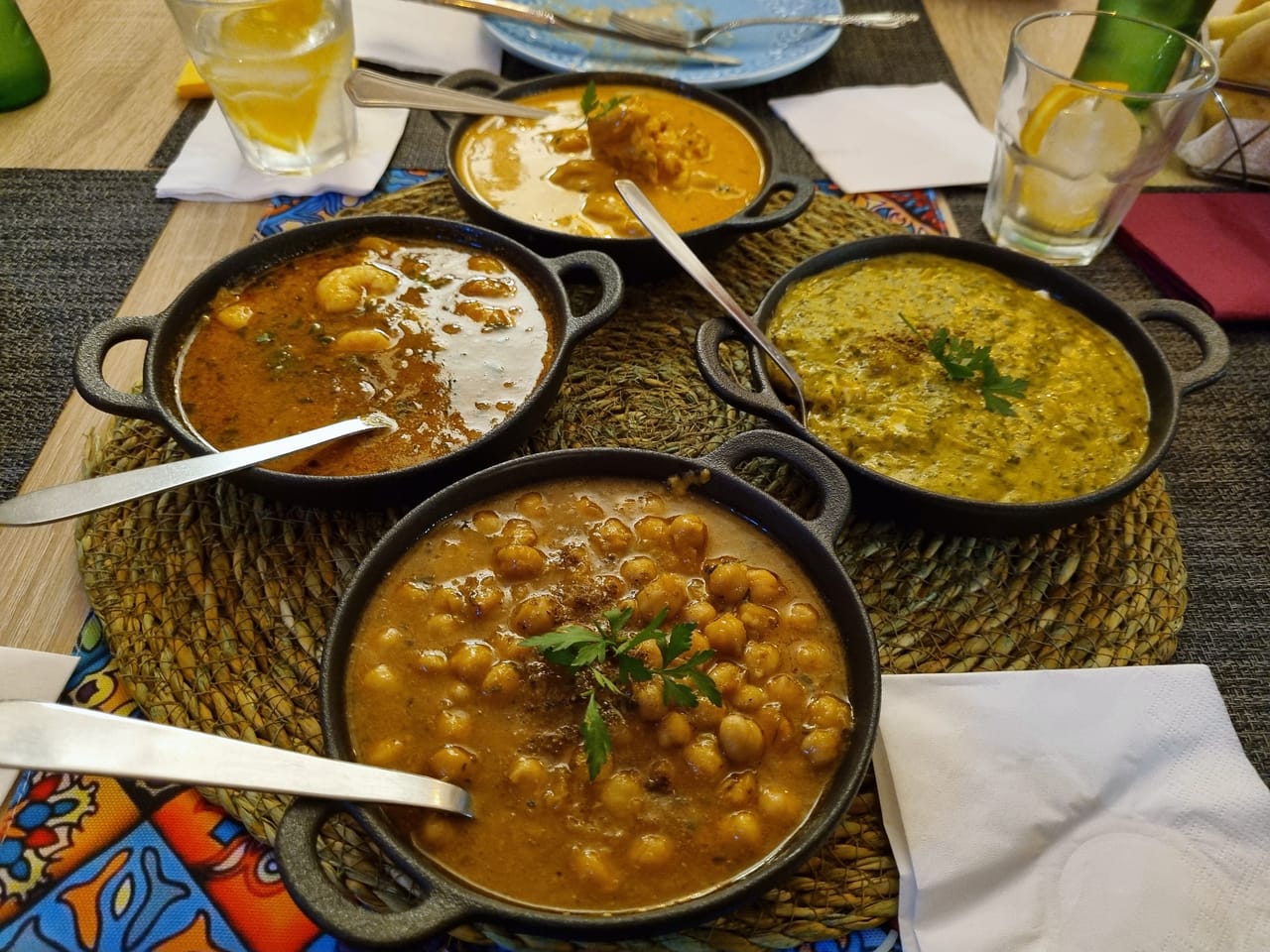 Quatro caris em panelas de ferro pretas: laranja cremoso, vermelho, verde e de grão