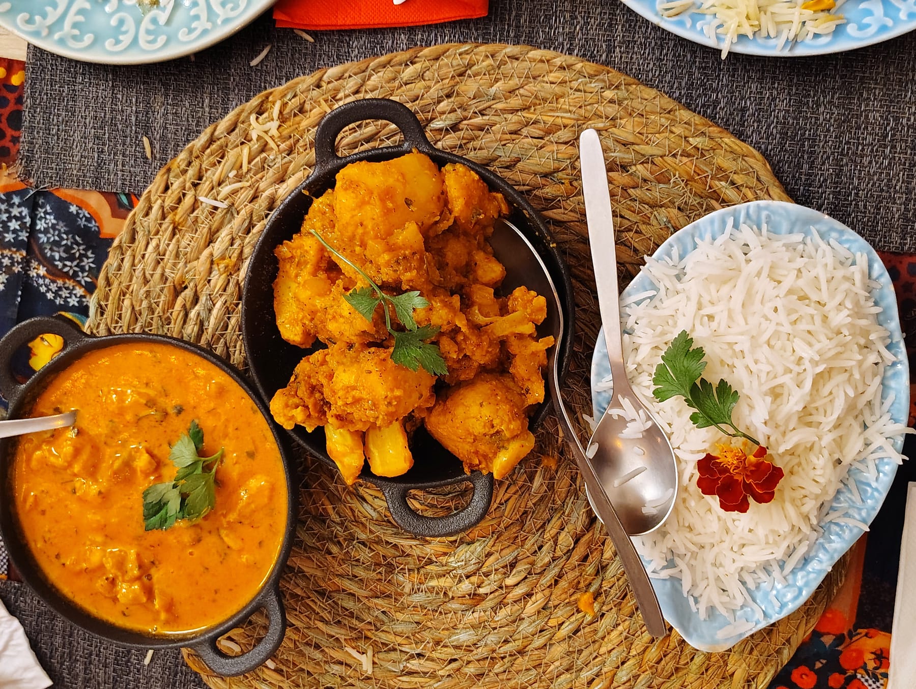 Caril cremoso numa panela de ferro, couve-flor e batata douradas noutra, e arroz basmati num prato azul claro
