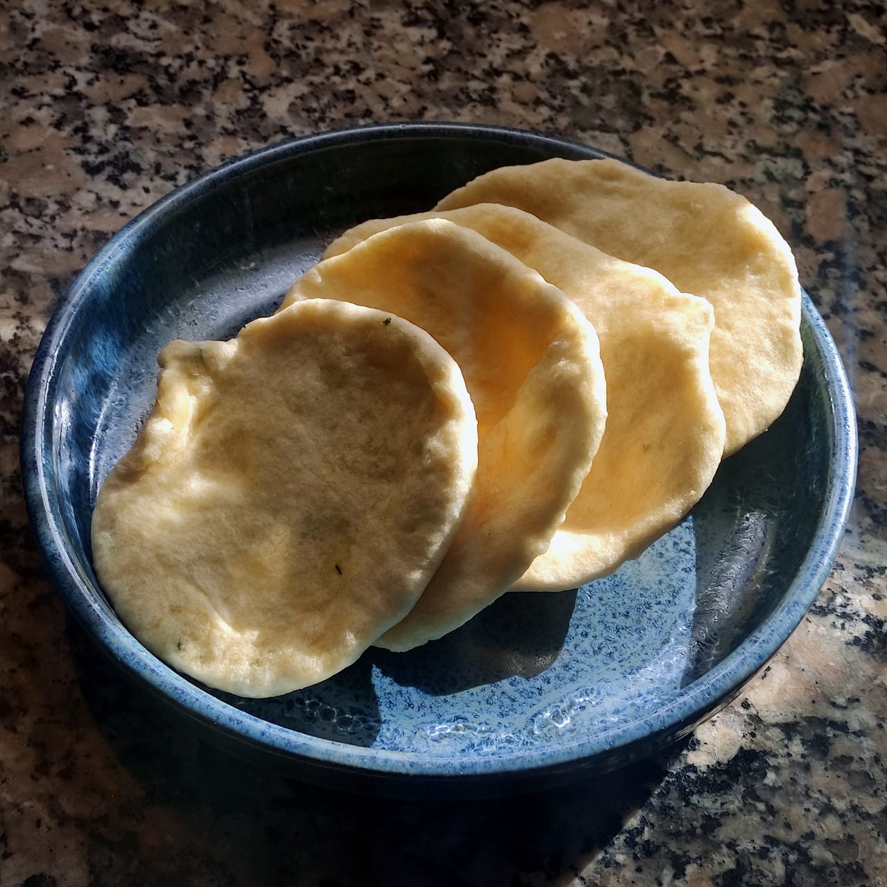 Quatro pães poori dourados numa taça de cerâmica azul salpicada