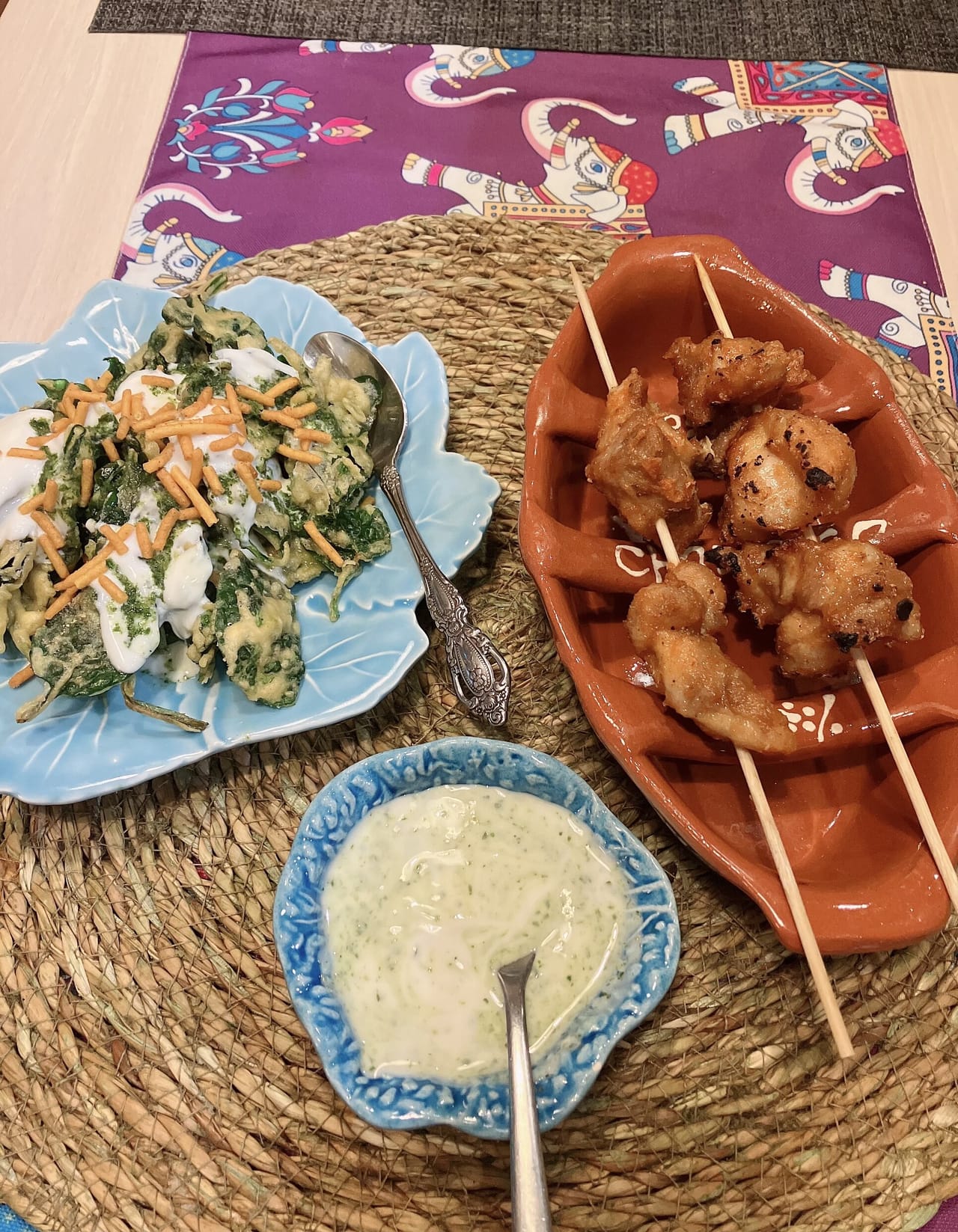 Espetadas de frango numa travessa de barro, pastéis de espinafres num prato azul e uma taça de molho de iogurte com ervas