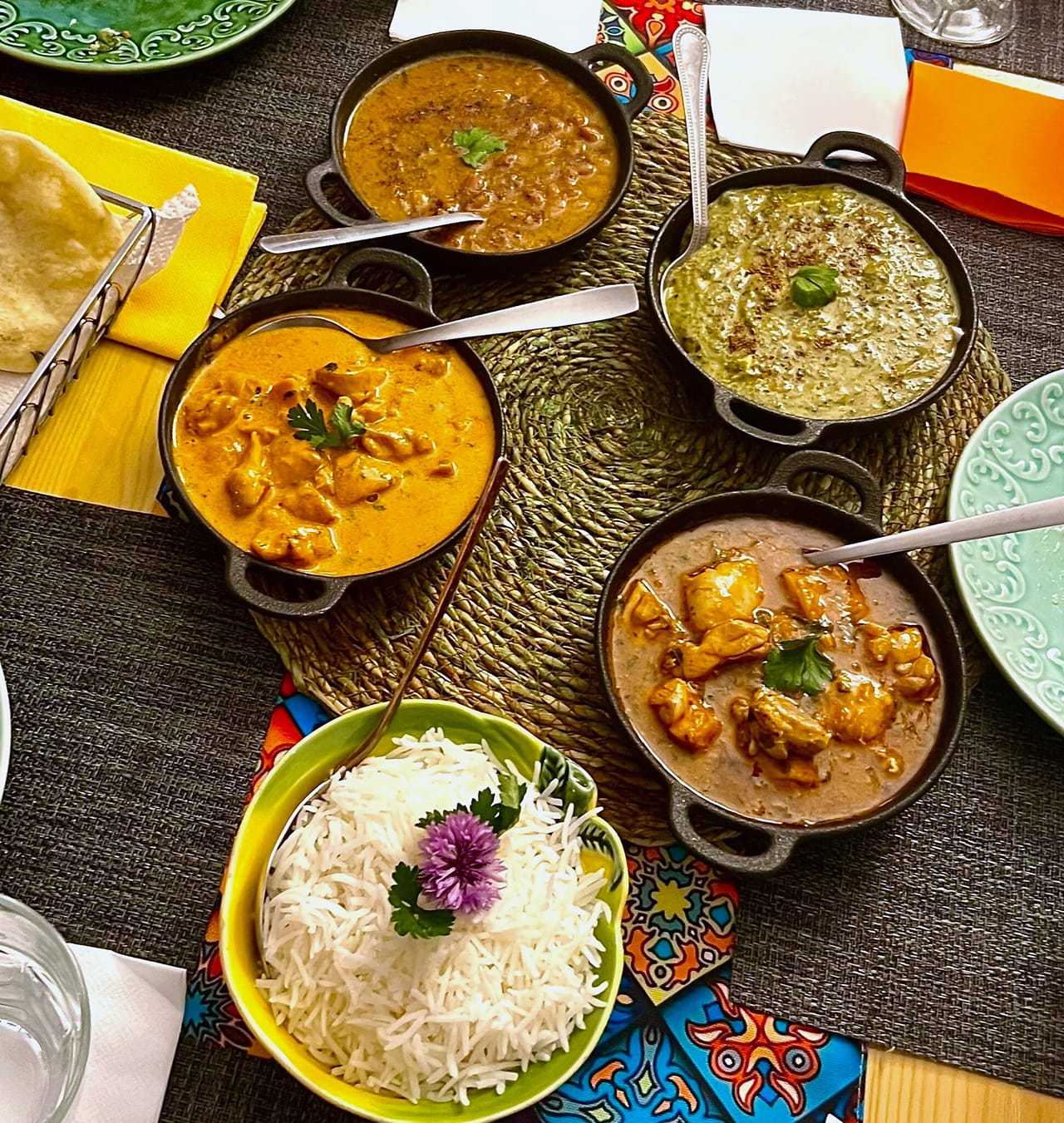 Mesa vista de cima com cinco panelas de caril, arroz basmati numa taça amarela e poori num cesto